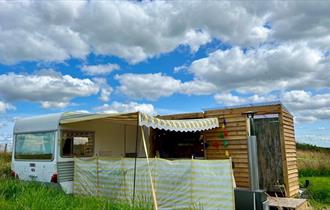 Outside view of vintage caravan with yellow awning, decking area and toilet/shower building