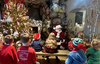 A group of children listening to Santa, telling a story beside a Christmas Tree