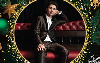 Singer, Alex Hall, reclining on a chair. Poster contains a border of Christmas baubles, stars, pine cones and glitter.