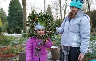 A child and an adult in the grounds of Ushaw peering through a handmade festive wreath.