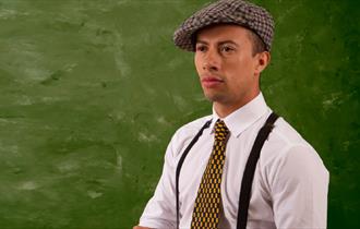 Someone wearing a flat cap and braces and chequerboard tie.