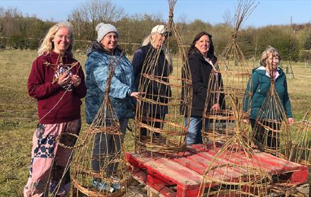 5 members of a willow weaving workshop at Dalton Moor Farm standing in front of their willow obelisks.