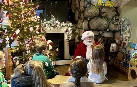 Children listening to Santa telling a story beside the Christmas Tree