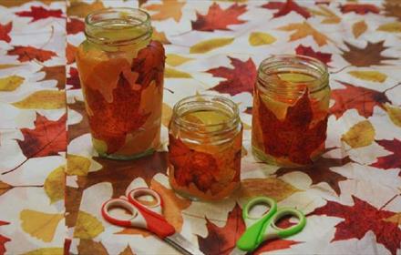 Leafy Lanterns at Ushaw. Jars with autumnal leaves in them, placed on a table with a leafy patterned tablecloth.