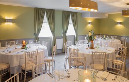 Dining room set out with round tables with white tablecloths, white chairs and table settings