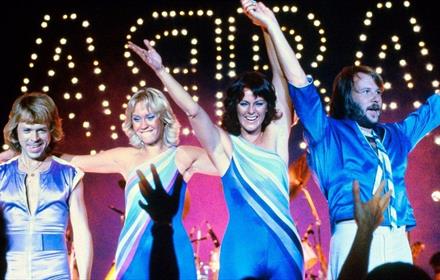 Image of the band, 'ABBA' holding hands on stage and waving to a crowd.