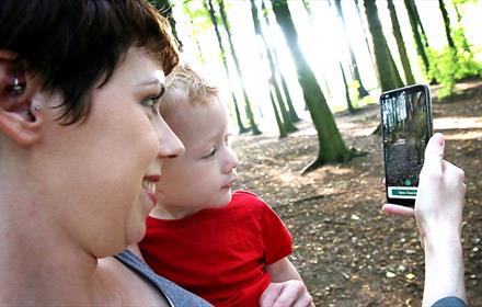 Woman with child looking at App on a mobile phone, forest setting