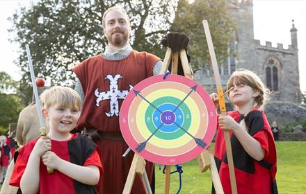An archery target with two children holding bow and arrows with the instructor