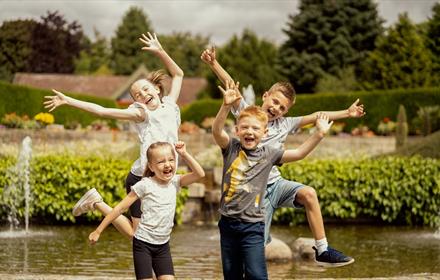 Four children laughing and jumping in the air in front of a pond at Durham University Botanic Garden.
