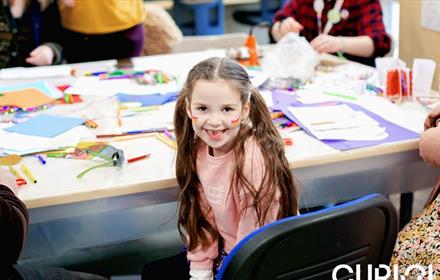 Child with rainbows painted on her face doing arts and crafts