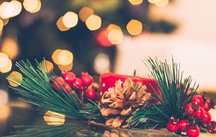 Christmas centrepiece showing holly, pine cone and red candle.