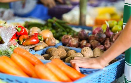 Close up of vegetables at market stall. Person standing next to veg.