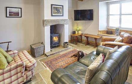 Cosy living are in cottage with real log burner, stone tiled floor and green leather sofa. Wooden beams on the ceiling.