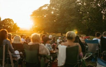 Image of an audience enjoying Open Air Theatre at Raby Castle as the sun sets.