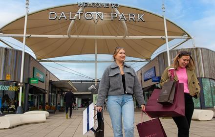 Shoppers leaving Dalton Park Outlet and Outdoors with lots of bags, smiling.