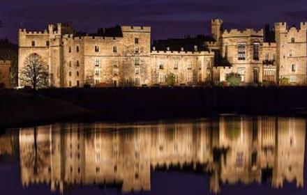 Image of Raby Castle at Dusk, softly lit. The reflection of the castle can be seen in the lake.