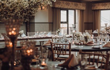 The Orangery, with friendly folk pelmets, soft grey ticking curtains, lime-washed furniture, and clothed tables with floral centrepieces and candles.