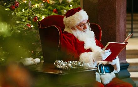 Father Christmas reading a book beside the Christmas Tree