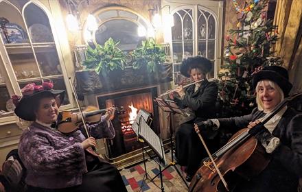 People in period dress, playing instruments by the Christmas Tree at Beamish Museum