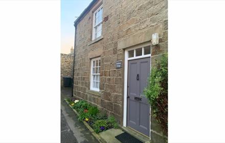 Exterior of Firethorn cottage. A stone building with grey wooden door