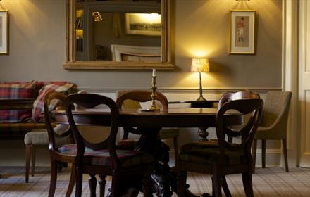 Dark wooden dining table with four chairs with a single candlestick in the centre. The room has a tartan carpet with green walls.