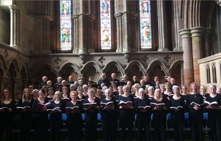 Altrincham Choral Society performing together in a beautiful church with colourful stained glass windows.