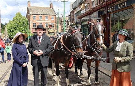 People in period dress stand beside two horses