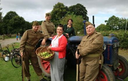 People dressed in army/1940s clothing, leaning against a tractor
