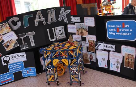 Engineering and maths-related activities in front of a sign which reads, 'Crank It Up!'