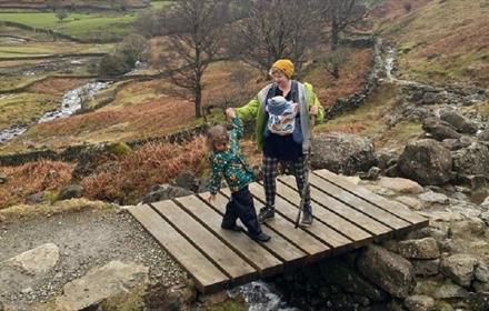 Woman with small child and baby, stood on a wooden footbridge in the North Pennines