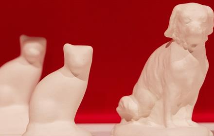A blank cat and dog bisque figurine on a white shelf with a pink background