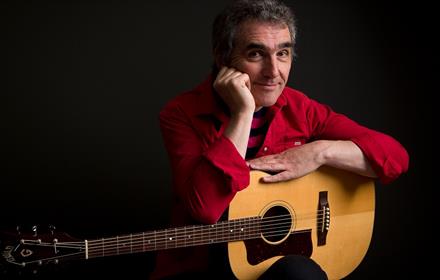 Photo of Jez Lowe wearing a red shirt with a guitar