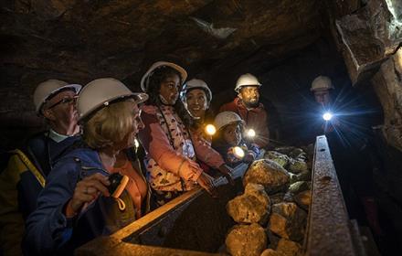 Children wearing hard hats in Killhope Lead Mine in dark truck full of rocks