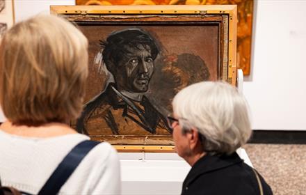 Two women with grey hair looking at a self portrait by Norman Cornish