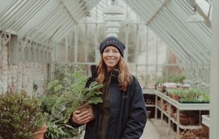A woman standing in the greenhouse and holding a plant at Raby Castle