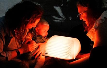 Two adults and a baby looking at an illuminated open book