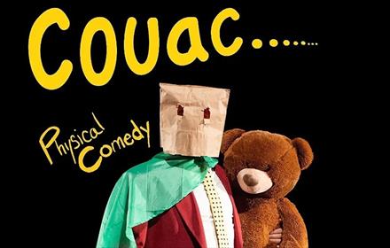 person wearing a suit with a green cape, a brown paper bag on head, holding a teddy bear