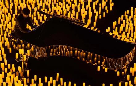 Someone playing a grand piano surrounded by lit candles