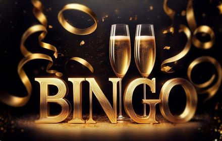 Two glasses of champagne with a stand spelling out BINGO in gold letters and gold ribbon.