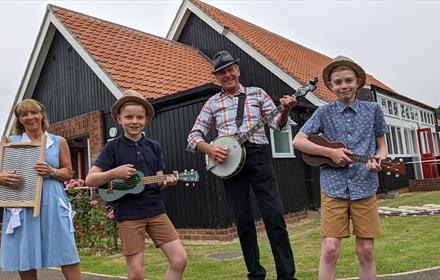 A Skiffle group of two adults and two children in front of Beamish Museum's 1950s welfare hall.