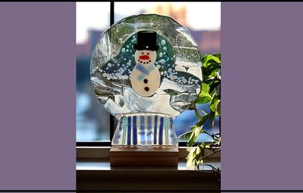 Fused glassed made into the shape of a snow globe with a Snowman design.