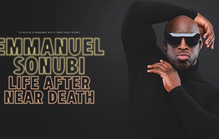 Emmanuel Sonubi wearing sunglasses and posing with one arm behind his head