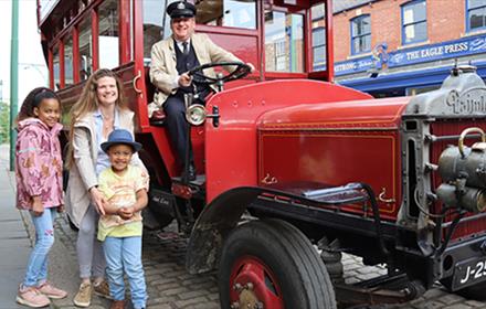 A family posing next to a traditional car at Beamish Museum.