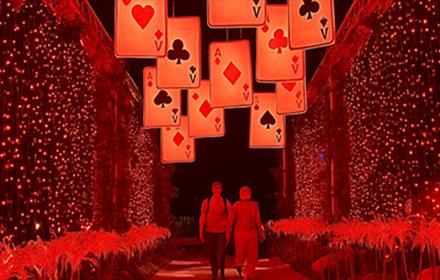 Adventures in Wonderland. Two people walking through a red tunnel of lights, beneath suspended playing cards.