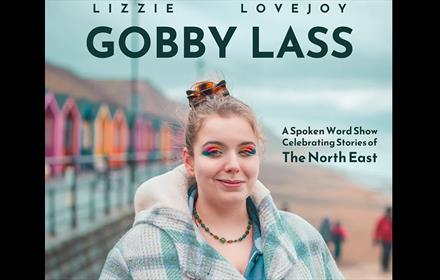 Lizzie Lovejoy, 'Gobby Lass' wearing colourful eyeshadow, standing at the beach, next to vibrant beach houses