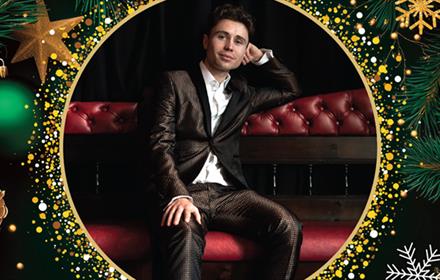 Singer, Alex Hall, reclining on a chair. Poster contains a border of Christmas baubles, stars, pine cones and glitter.