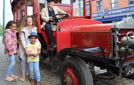 A family at Beamish Museum standing with a vintage bus being driven by a Transport Engager.
