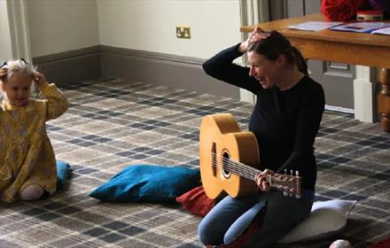 A little girl singing along to a woman playing the guitar.