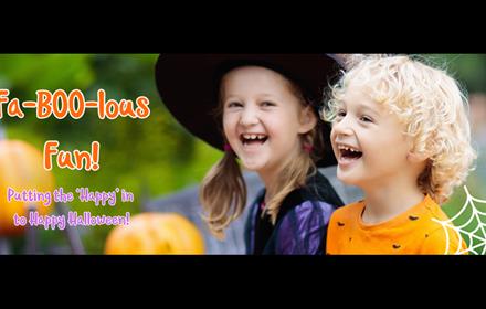 Children two children laughing. One dressed as a witch and the other wearing an orange top with a bat pattern.