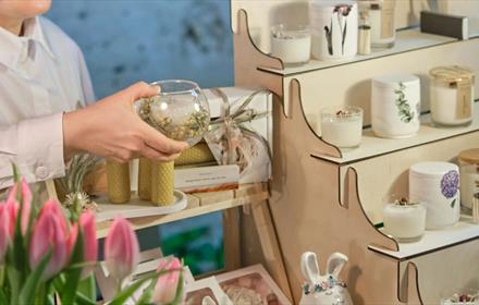 Local artisan craft at No.42, someone holding a bowl. There's a shelf showing a selection of candles and trinkets.